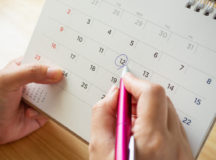 calendar page with female hand holding pen on desk table