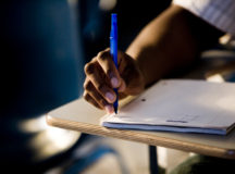 Close-up of a male student writing on book in the classroom