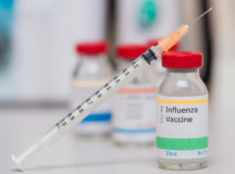 influenza vaccination concept with syringe in vaccine vial and other vials in background