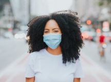 Young woman in the city smiling behind the coronavirus face protection mask