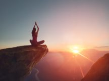 Woman practices yoga and meditates on the mountain.